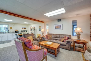 A living room with a sofa, armchair, coffee table, and a kitchen area in the background. - Anchorage Apt: Home Base for Alaska Adventure! (Anchorage)