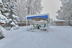 Zona d'estar a l'exterior coberta amb taula i cadires, envoltada d'arbres plens de neu i una tanca de fusta.