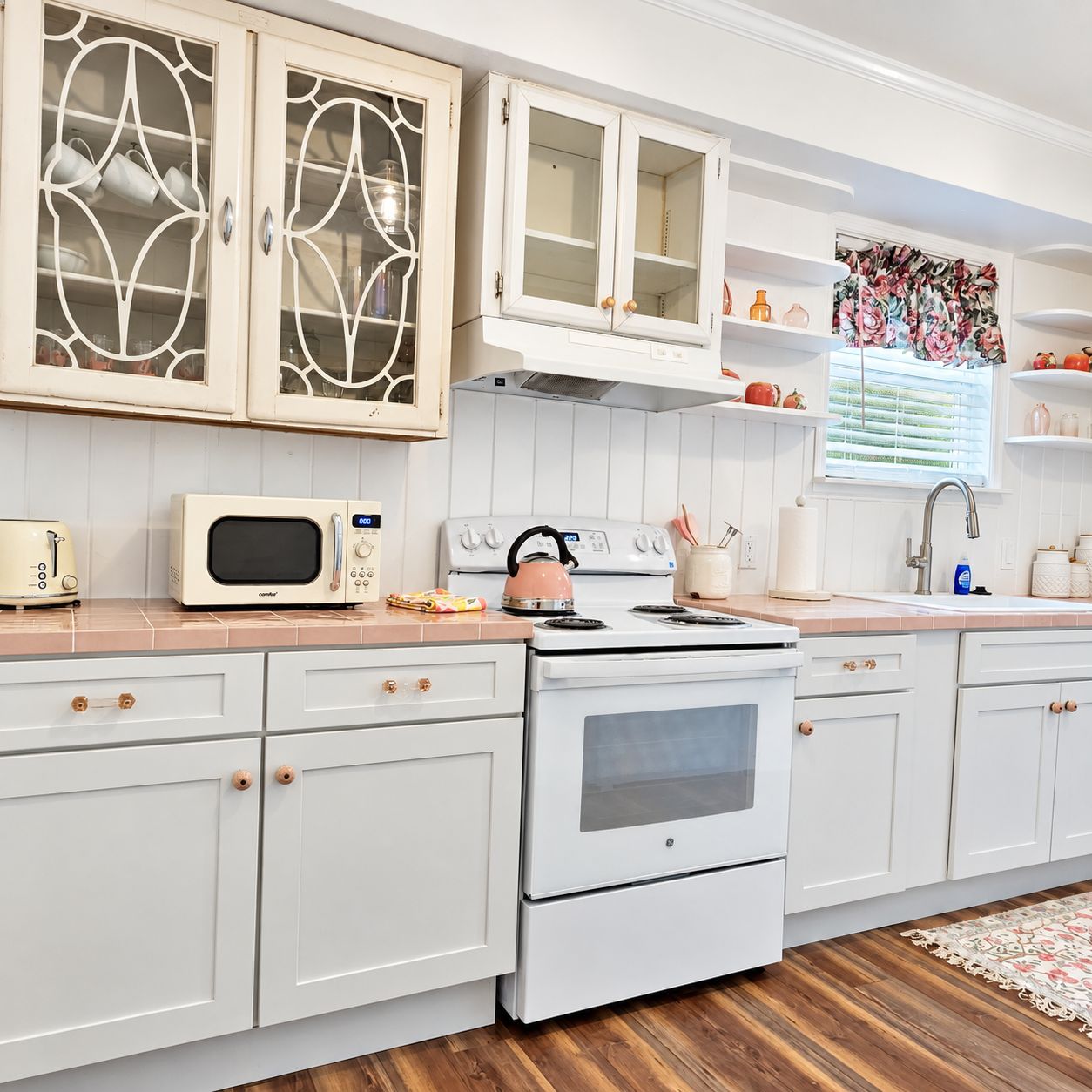A kitchen with white cabinetry, a microwave, a kettle, and a stove.