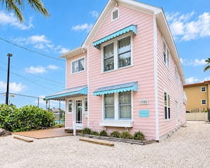A pink two-story house with a blue awning, a front porch, and a gravel driveway.
