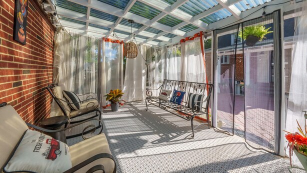 Un patio techado con un banco de metal, una silla acolchada y una planta en maceta.