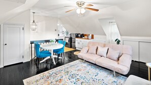 Un loft amplio con techos altos, un comedor con sillas azules, un sofá rosa y una cocina al fondo.