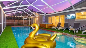 Ein überdachter Pool mit einer Schwimmswan in Goldfarbe, Liegestühlen, einem Whirlpool und einem Fernsehbildschirm.