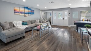 Ein geräumiges Wohnzimmer mit grauem Sofa, einem Glastisch und einem Essbereich mit schwarzem Tisch und Stühlen.