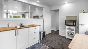 A compact kitchen with white cabinetry, a wooden countertop, a sink, a trash can, and a microwave on a white shelf. - Nine Acres - FREE Wi-Fi (Invercargill)