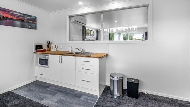 A modern kitchen with white cabinets, a wooden countertop, a built-in microwave, and a window above the sink. - Nine Acres - FREE Wi-Fi (Invercargill)