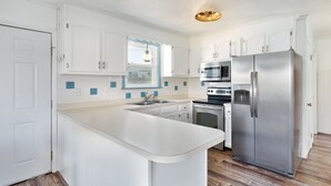 Una cuina moderna amb armaris blancs, un refrigerador d'acer inoxidable, un forn i un microones.