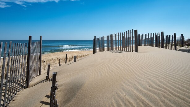 Platja de sorra amb una tanca de fusta i un cel blau clar.