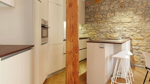 A modern kitchen with a stone wall, wooden beam, and white bar stools. - Salamanka by FeelFree Rentals (Donostia)