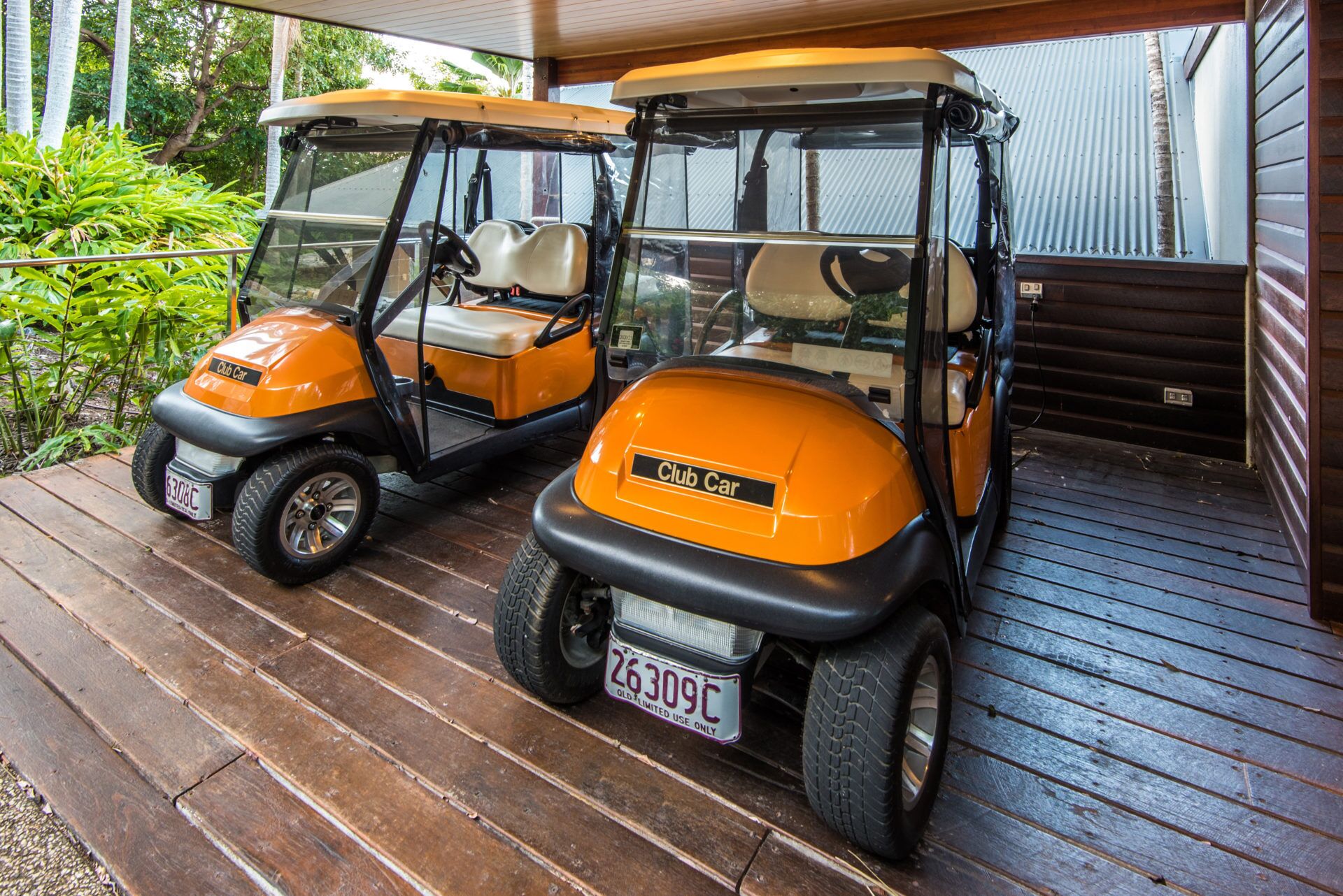 Due golf cart parcheggiate su un pontile di legno con ringhiera metallica e una casa sullo sfondo.