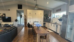 A modern kitchen with a central island, wooden flooring, and a dining area with chairs. - Horotiu Large Group Accommodation & Events (Horotiu)