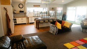 A modern living room with a leather sofa, a zebra-patterned armchair, and a colorful rug. There is a kitchen area with white cabinets and a microwave on the counter. - Horotiu Large Group Accommodation & Events (Horotiu)