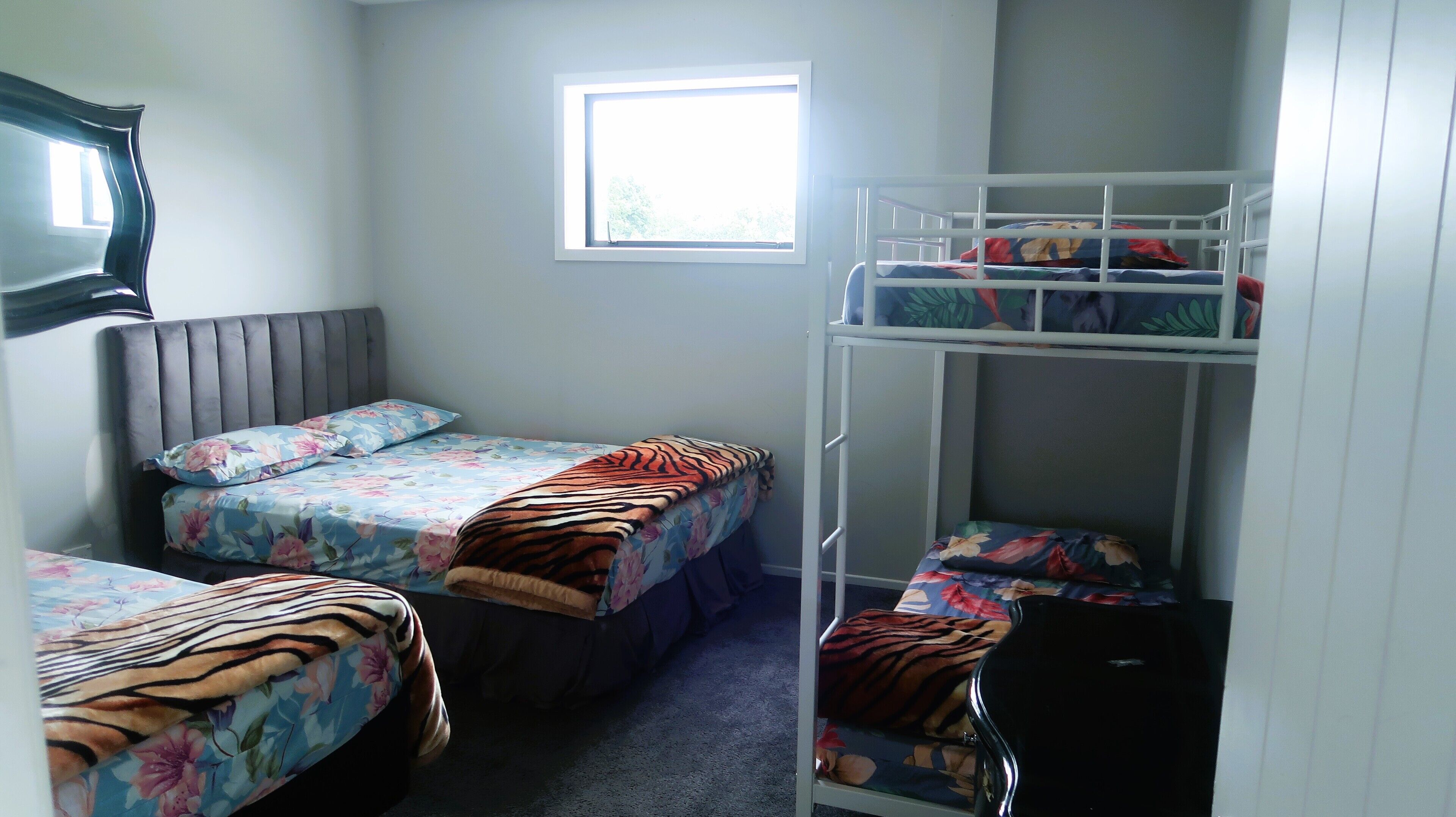 Een slaapzaal met twee eenpersoonsbedden, een stapelbed, een raam en een televisie aan de muur.
