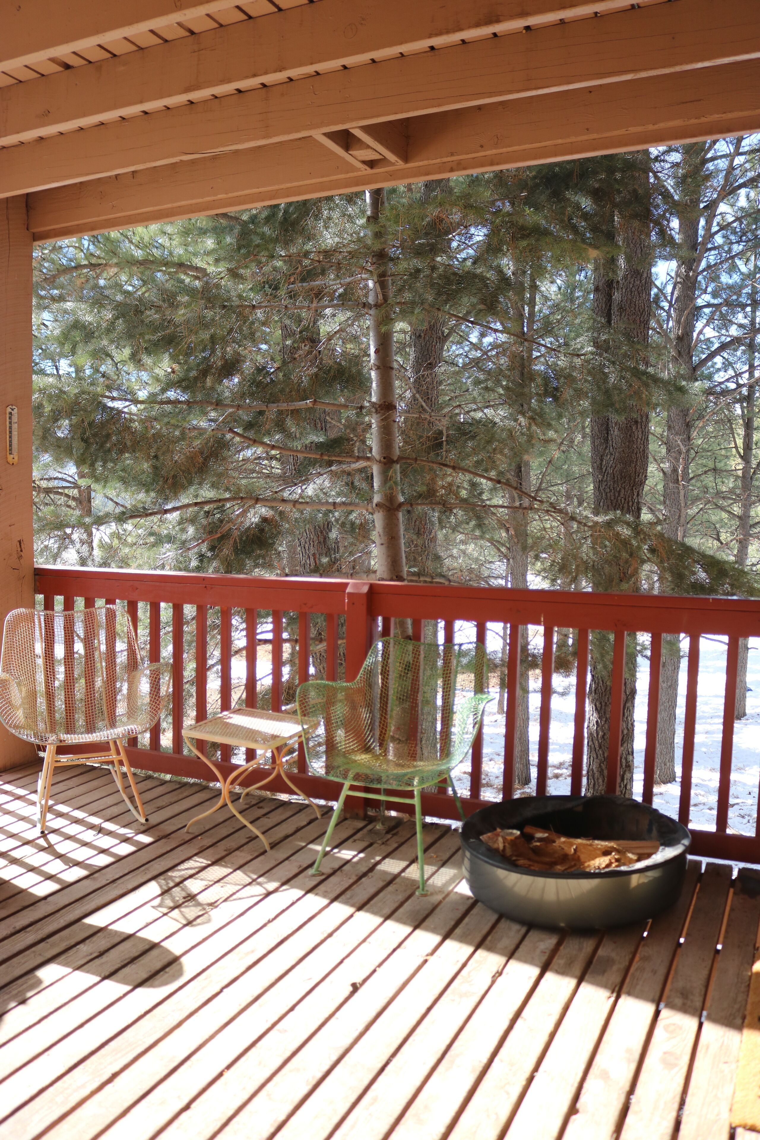A wooden deck with a red railing, two wicker chairs, and a metal fire pit.