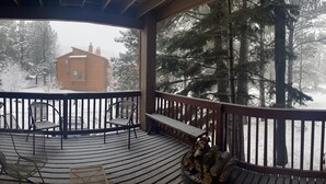 Een houten terras met een bank en stoelen, met uitzicht op een besneeuwd bos en een blokhut.