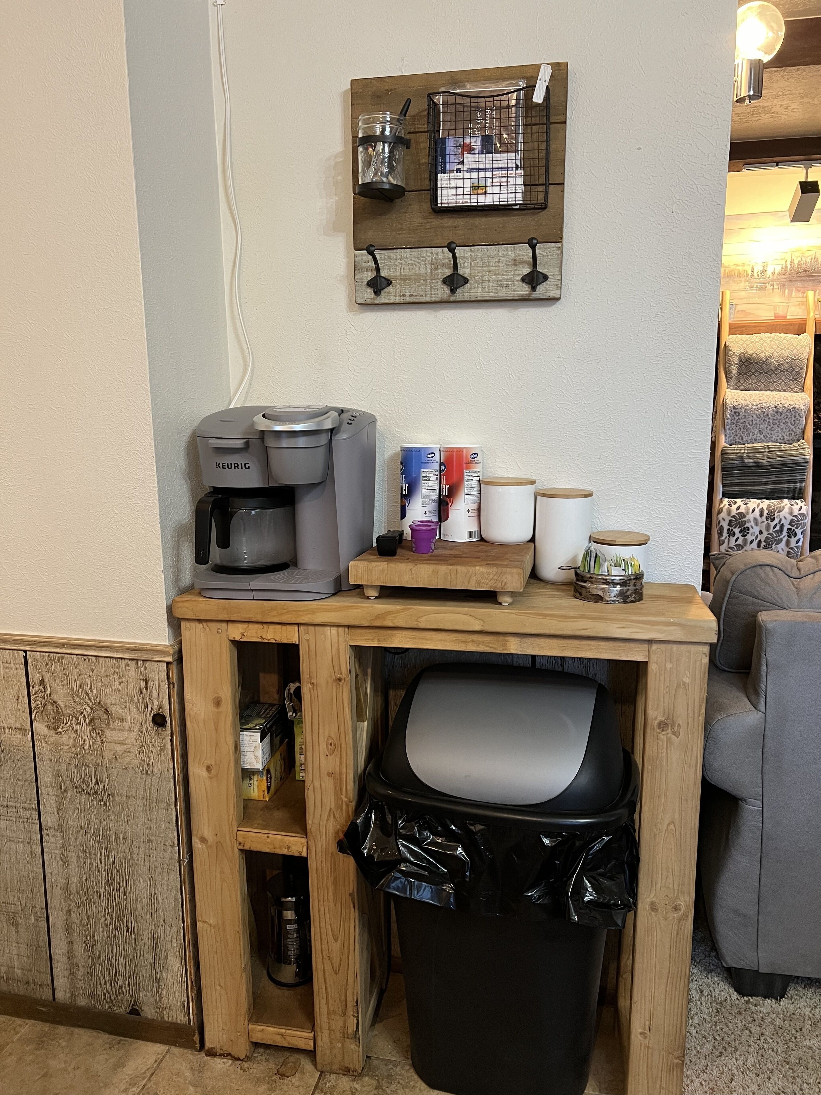 Una kitchenette con cafetera, tazas de café y un cubo de basura.