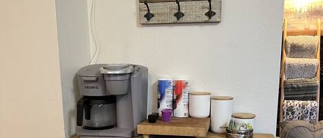 A kitchenette with a coffee maker, coffee cups, and a trash bin.