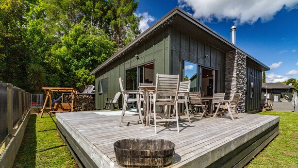 Um deck de madeira com mobiliário de exterior, uma lareira de pedra e uma janela grande.