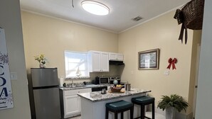 A modern kitchen with white cabinets, a central island with stools, a refrigerator, and a microwave. - 🌹Southern’s Beauty 1🌹 (Kenner)