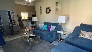 A living room with a blue sofa, a coffee table, and a dining area with chairs and a table. - 🌹Southern’s Beauty 1🌹 (Kenner)