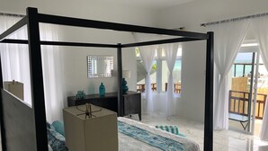 A four-poster bed with a white and blue patterned bedspread, a bedside table with a lamp, and a dresser with decorative items.