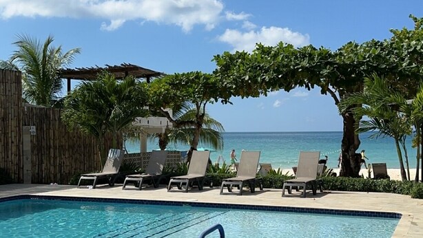 A pool area with lounge chairs and a view of the ocean.