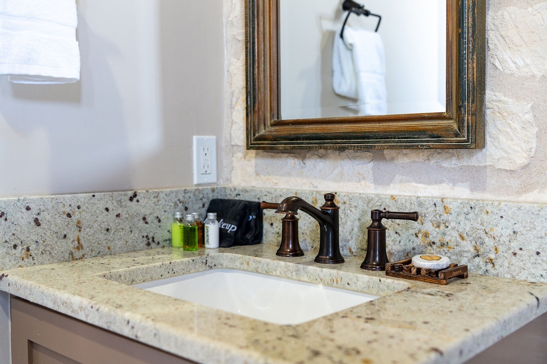 A bathroom with a granite countertop, a white sink, and a mirror with a wooden frame.