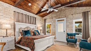Un dormitorio con una cama grande, ventilador de techo, paredes de piedra y vistas al exterior.