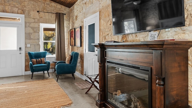 Una habitación acogedora con pared de piedra, chimenea y dos sillones azules.