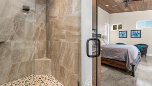 Een moderne badkamer met een douchecabine van glas, een houten plafondventilator, en een slaapkamer met een bed en kunst aan de muur.