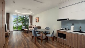 Una cocina moderna con armarios de madera, un comedor con una mesa redonda y sillas, y un amplio ventanal con vistas a palmeras.