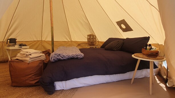 A tent with a bed, pillows, a table, and a chair.