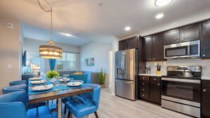Une cuisine moderne avec des meubles en bois foncé, des appareils en acier inoxydable et un coin repas avec des chaises bleues et une table en bois, le tout disposé pour accueillir quatre personnes.