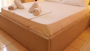 A neatly made bed with white linens and rolled towels, a beige headboard, and an air conditioning unit on the wall. - Charming 2-Bed Apartment in Sarandë (Sarande)