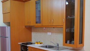 A compact kitchen with wooden cabinets, a built-in oven, a refrigerator, and a sink. - Charming 2-Bed Apartment in Sarandë (Sarande)