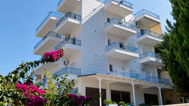 Ein mehrstöckiges Hotel mit Balkonen, einem überdachten Eingang und umgebender Bepflanzung.