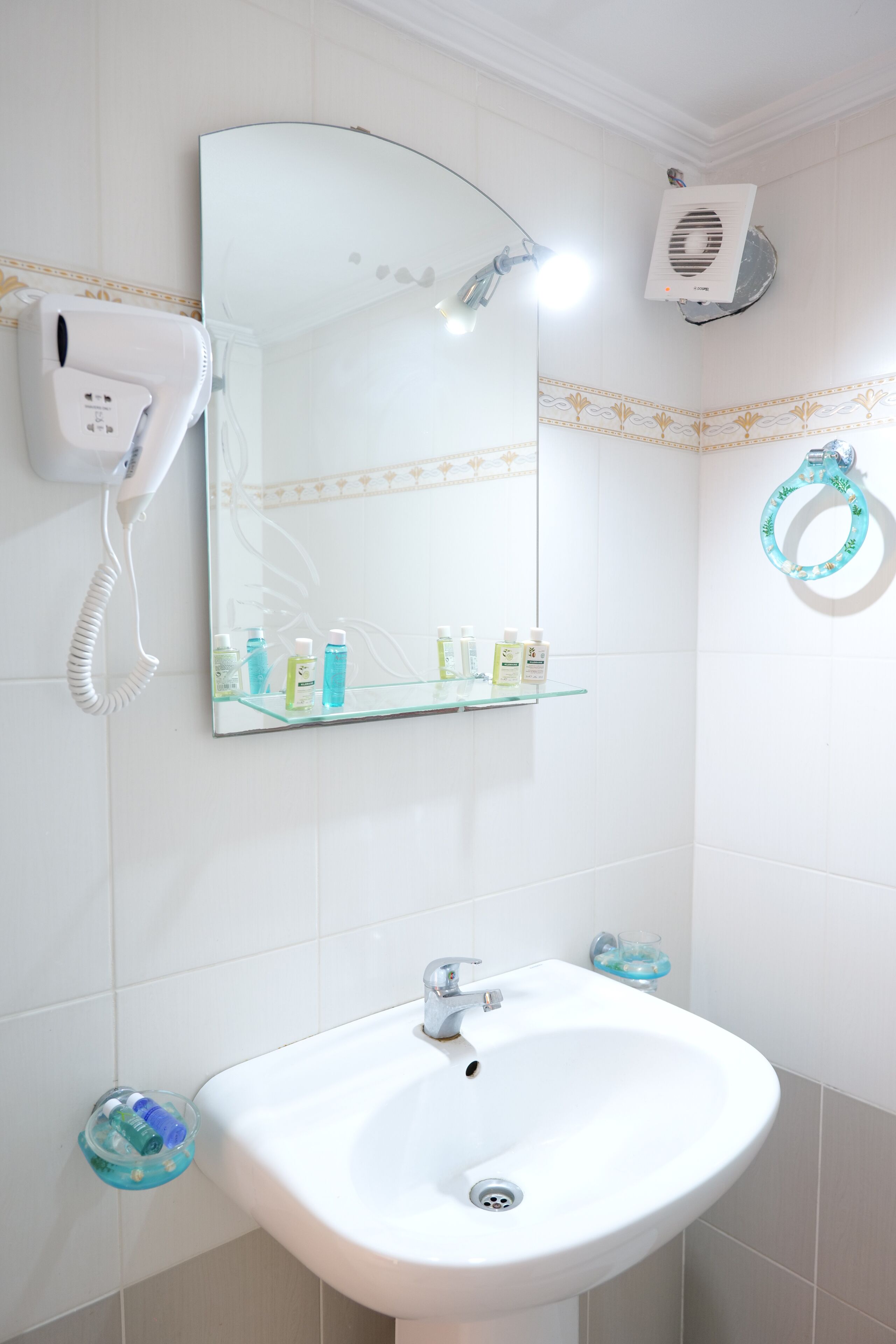A bathroom with a white sink, a mirror, a hairdryer, and a towel ring.