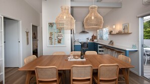Eine moderne Küche mit weißen Schränken, einem Holztisch, Korbstühlen und Pendelleuchten.