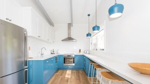 Eine moderne Küche mit blauen Schränken, weißen Arbeitsflächen, einem Edelstahlkühlschrank und Holzbarhocker.