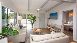Ein geräumiges Wohnzimmer mit einem großen Fenster, einem Deckenventilator und einem Bett im angrenzenden Raum.