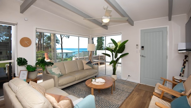 Ein geräumiges Wohnzimmer mit großem Fenster, Deckenventilator und Meerblick.