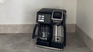 A kitchen with a coffee maker, glass mugs, and a framed sign on the wall.