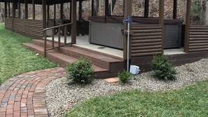 A covered outdoor area with a wooden structure, steps leading up to a bench, and a small garden area with a brick path.