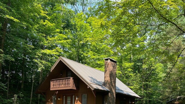 A cabin with a balcony, surrounded by a gravel path and a wooden fence.