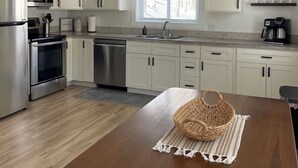 A modern kitchen with white cabinets, stainless steel appliances, a wooden table, and a chandelier.