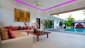 A modern living room with a large sofa, a wooden coffee table, and a ceiling fan. There is a pool visible in the background. - Elegant Private Villa, 3 BR, Seminyak With Staff (Keroboken Kelod)