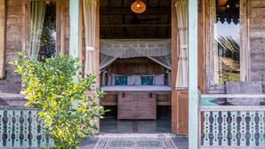 A rustic wooden cabin with a bed under a canopy, a hanging light fixture, and a small porch area.