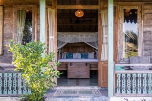 Una cabana de fusta rústica amb un llit sota una tònia, una làmpada penjant i un petit porxo.