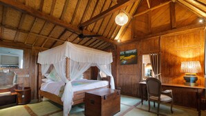 A room with a wooden ceiling, a four-poster bed with a canopy, a desk with a chair, and a painting on the wall.