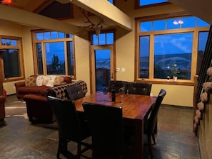 Relax in this spacious living area with a high ceiling and large windows offering a view of the outdoors. Enjoy meals at the dining table for four, accompanied by comfortable seating.